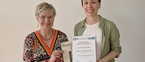 Julia Winkler (rechts im Bild) erhält eine Urkunde von Dekanin Prof. Andrea Kübler (links im Bild). Beide lächeln freundlich in die Kamera